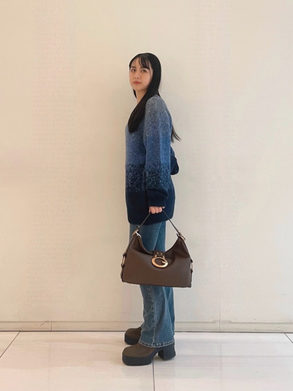 ブルー系のデニムパンツ、ブラウン系のショルダーバッグ、ブルー系のニット/セーターを着用したレディースの秋コーディネートの3枚目の写真