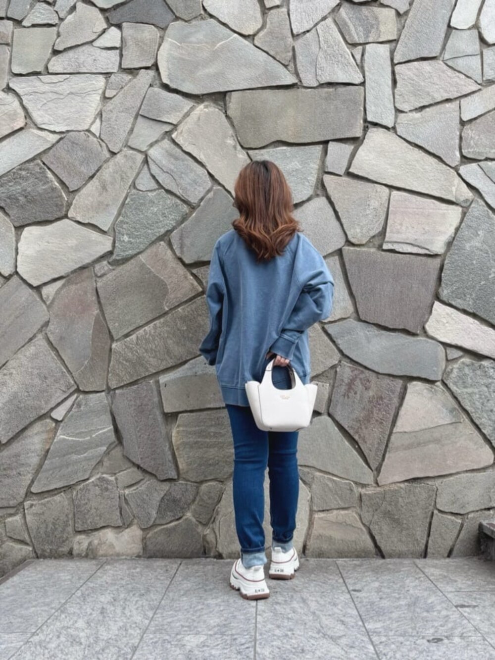 ブルー系のデニムパンツ、ホワイト系のショルダーバッグ、ブルー系のスウェットを着用したレディースの秋コーディネートの2枚目の写真