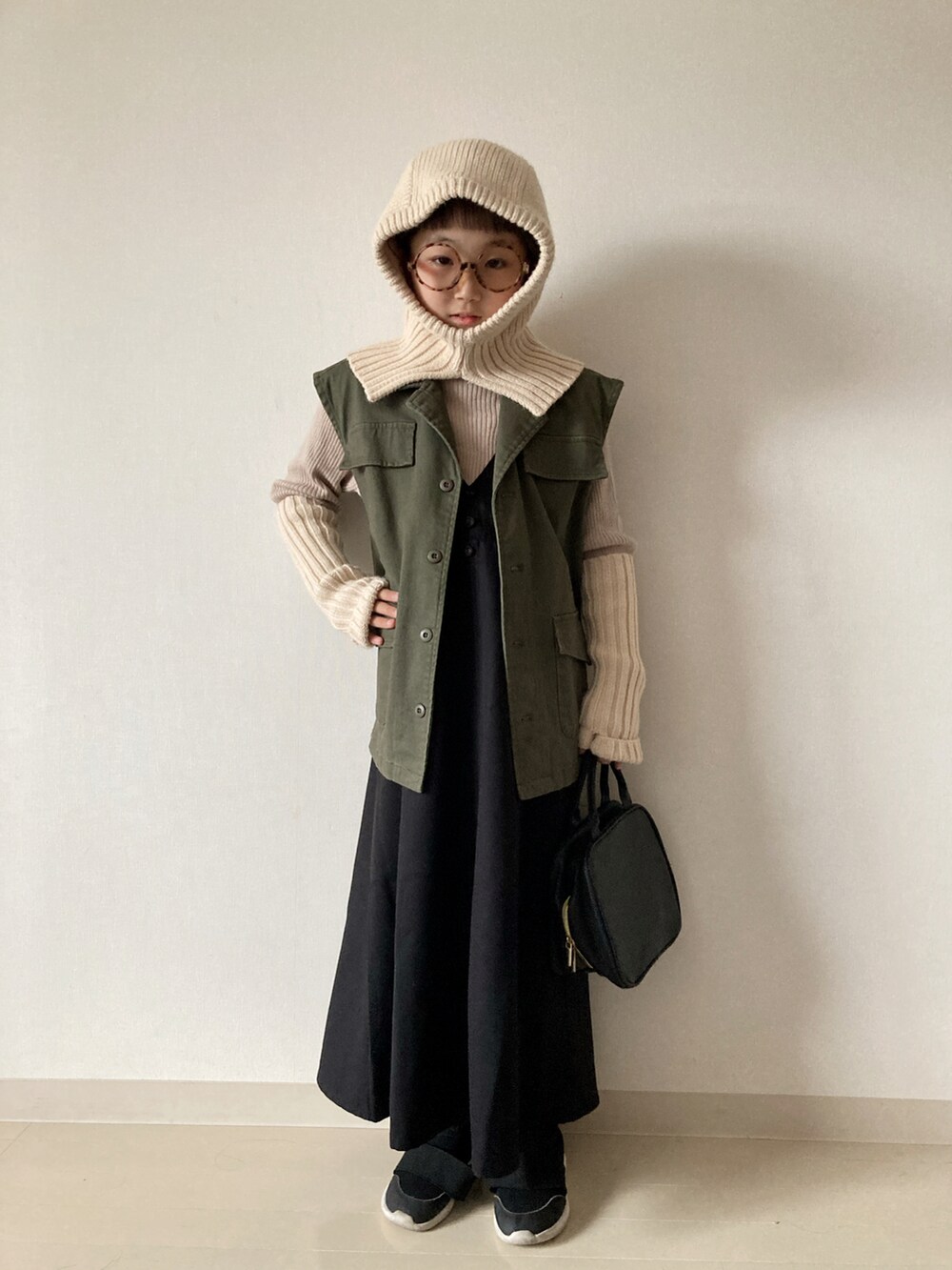 ブラック系のジャンパースカート、ベージュ系のニット/セーター、ブラック系のスニーカーを着用したキッズの秋コーディネートの2枚目の写真