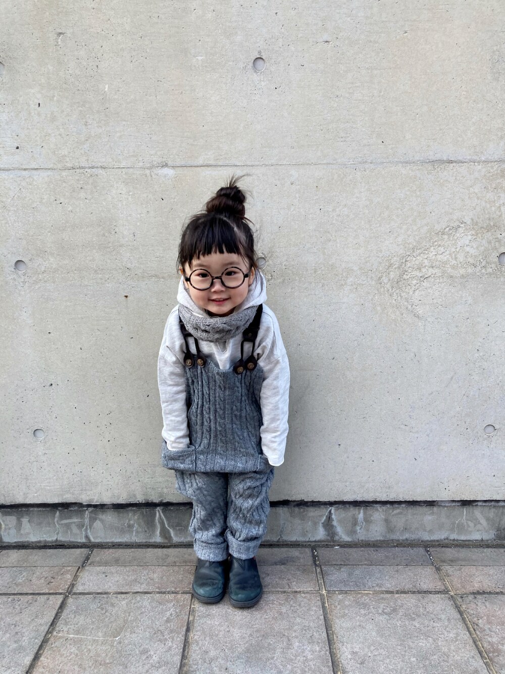 レッド系のブーツ、グレー系のサロペット/オーバーオール、ブラック系のニット/セーターを着用したキッズの冬コーディネートの2枚目の写真