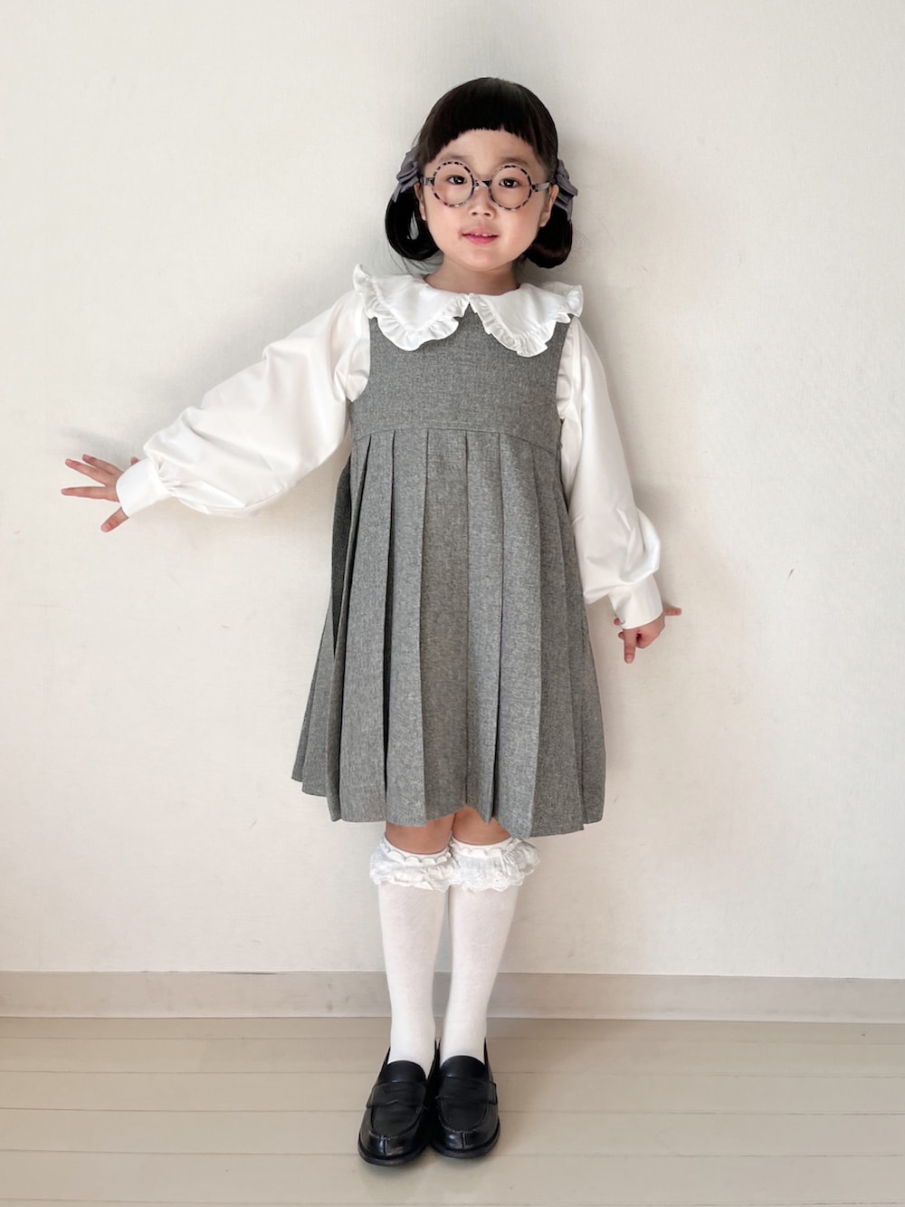 グレー系のジャンパースカート、ホワイト系のシャツ/ブラウス、ブラック系のローファーを着用したキッズの冬コーディネートの2枚目の写真
