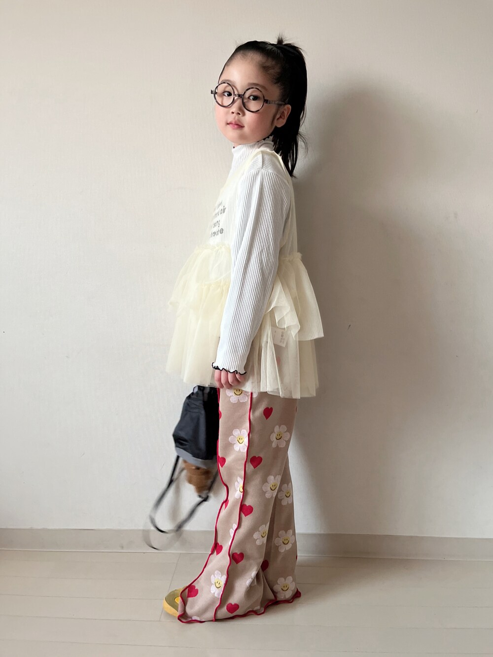 イエロー系のTシャツ/カットソー、ホワイト系のパンツ、ブラック系のショルダーバッグを着用したキッズの冬コーディネートの3枚目の写真