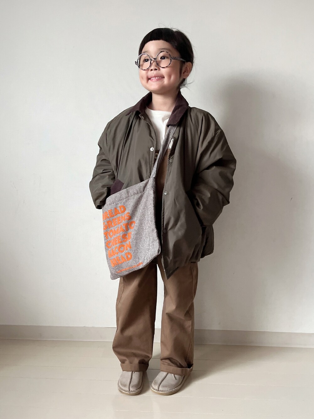 グリーン系のブルゾン、ホワイト系のTシャツ/カットソー、ブラウン系のショルダーバッグを着用したキッズの秋コーディネートの3枚目の写真