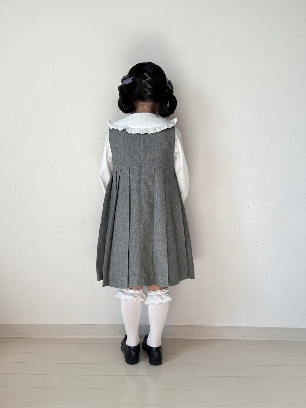 グレー系のジャンパースカート、ホワイト系のシャツ/ブラウス、ブラック系のローファーを着用したキッズの冬コーディネートの5枚目の写真