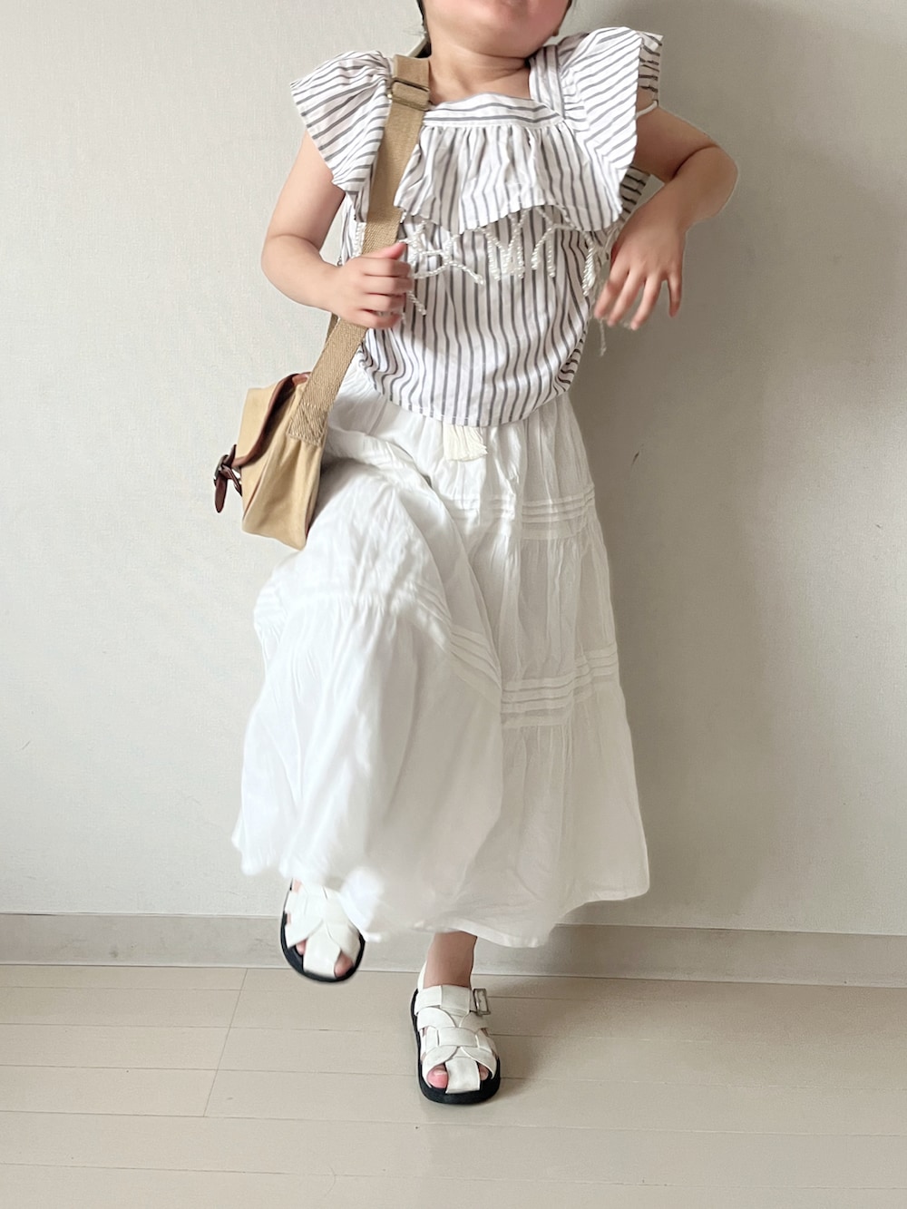 ホワイト系のスカート、ベージュ系のショルダーバッグ、ブラック系のセットアップを着用したキッズの夏コーディネートの4枚目の写真