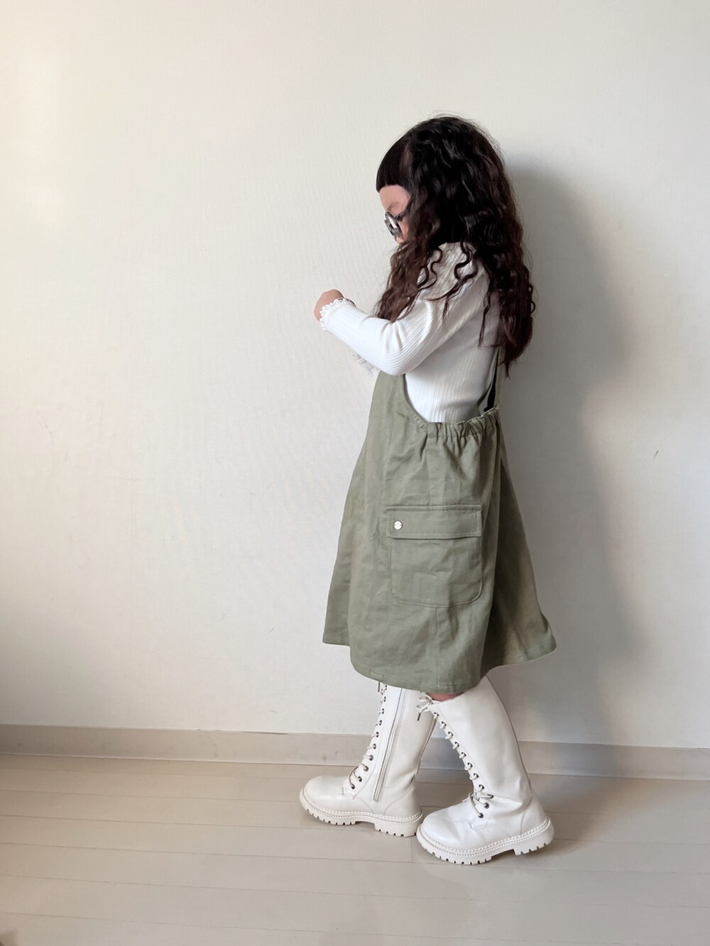 グリーン系のジャンパースカート、ベージュ系のTシャツ/カットソー、ホワイト系のカーディガン/ボレロを着用したキッズの冬コーディネートの3枚目の写真