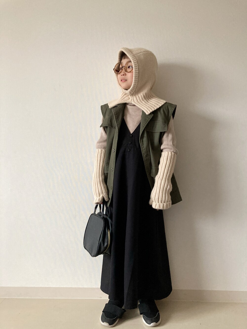 ブラック系のジャンパースカート、ベージュ系のニット/セーター、ブラック系のスニーカーを着用したキッズの秋コーディネートの4枚目の写真