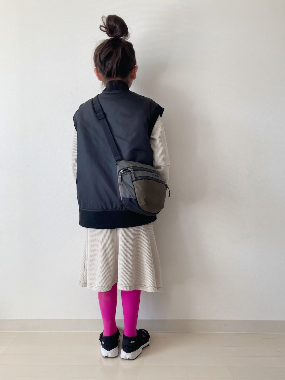 ベージュ系のワンピース、ブラック系のダウンベスト、ブラック系のスニーカーを着用したキッズの秋コーディネートの5枚目の写真