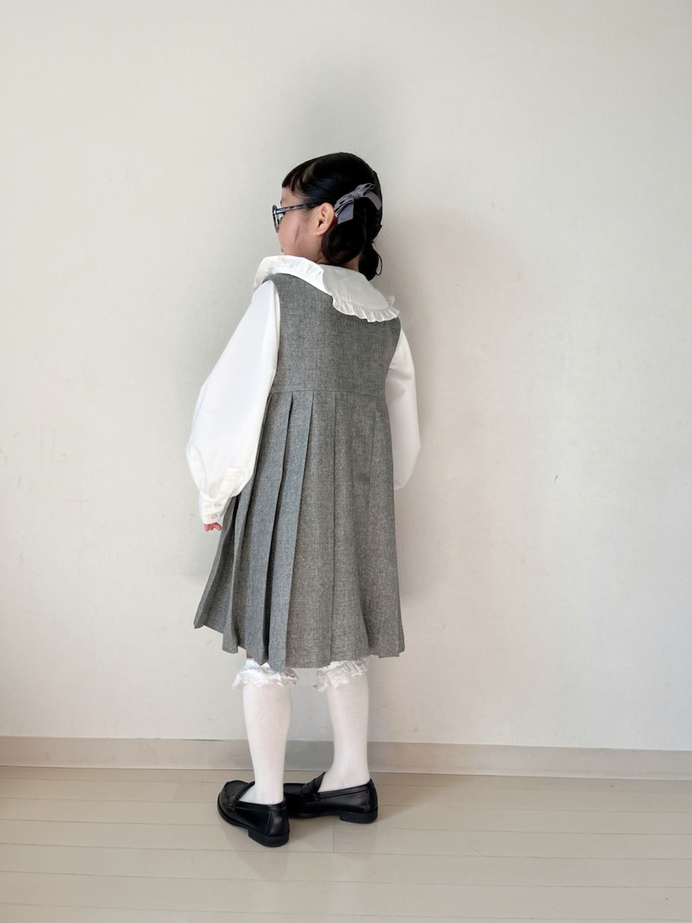 グレー系のジャンパースカート、ホワイト系のシャツ/ブラウス、ブラック系のローファーを着用したキッズの冬コーディネートの4枚目の写真