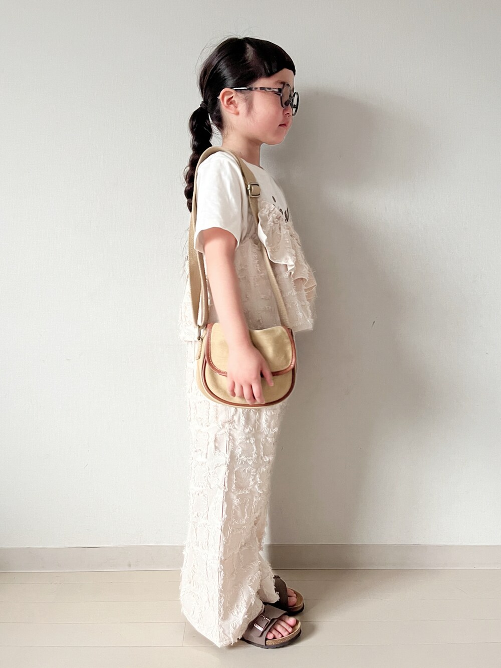 ベージュ系のショルダーバッグ、ブラウン系のサンダル、ベージュ系のTシャツ/カットソーを着用したキッズの春コーディネートの3枚目の写真