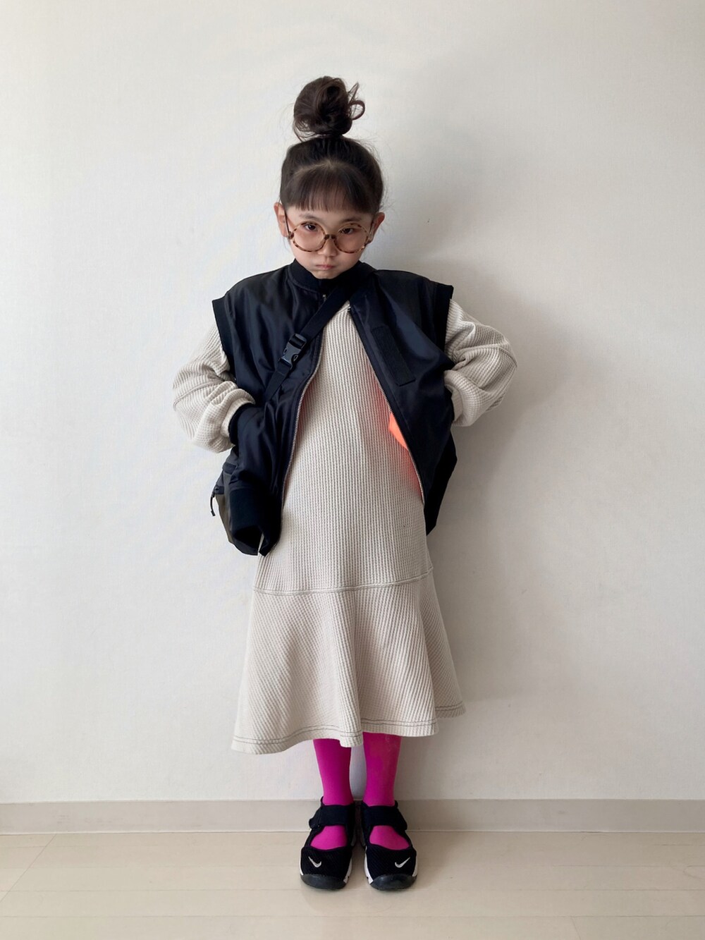 ベージュ系のワンピース、ブラック系のダウンベスト、ブラック系のスニーカーを着用したキッズの秋コーディネートの3枚目の写真