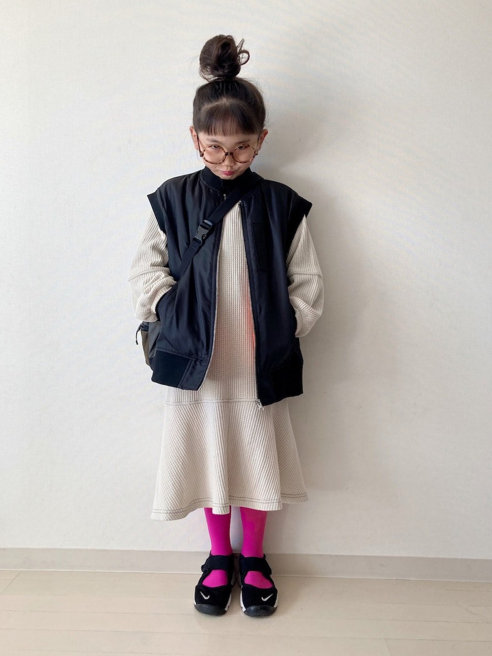 ベージュ系のワンピース、ブラック系のダウンベスト、ブラック系のスニーカーを着用したキッズの秋コーディネートの2枚目の写真