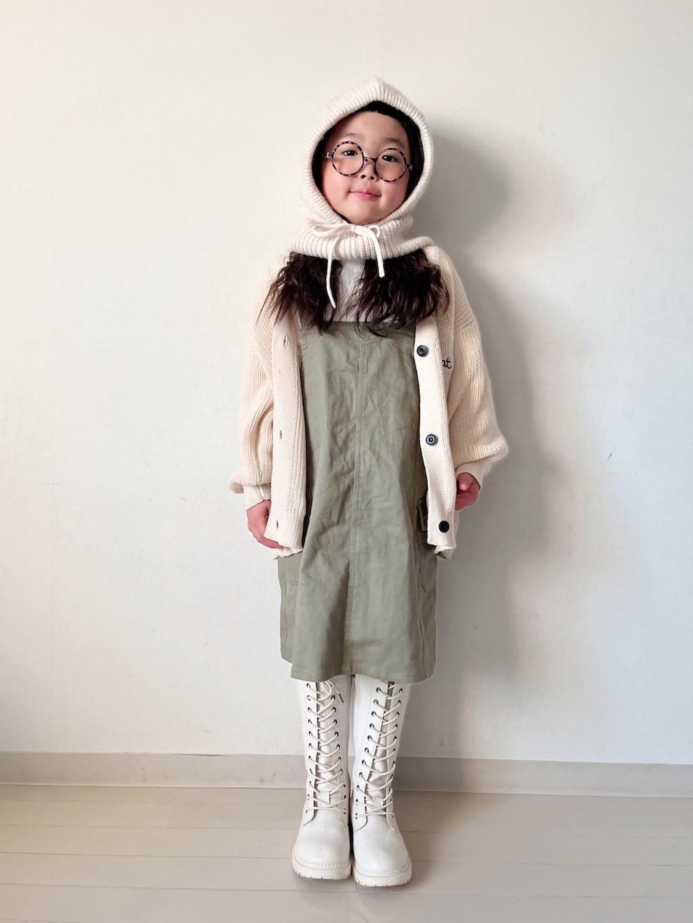グリーン系のジャンパースカート、ベージュ系のTシャツ/カットソー、ホワイト系のカーディガン/ボレロを着用したキッズの冬コーディネートの5枚目の写真