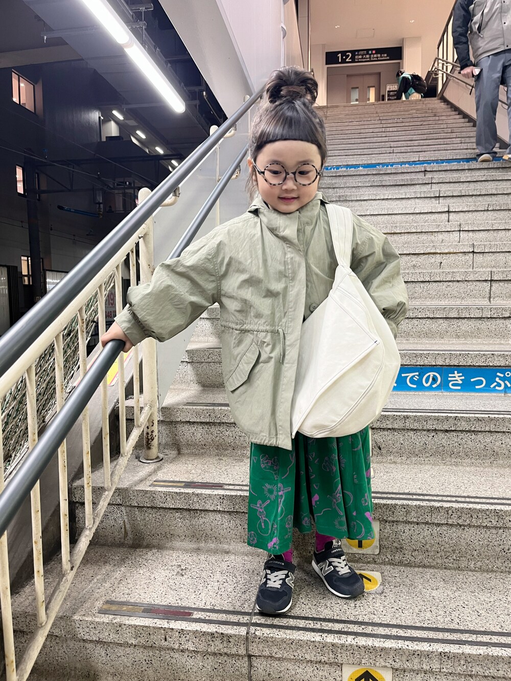 グリーン系のワンピース、ホワイト系のショルダーバッグ、グリーン系のステンカラーコートを着用したキッズの春コーディネートの2枚目の写真