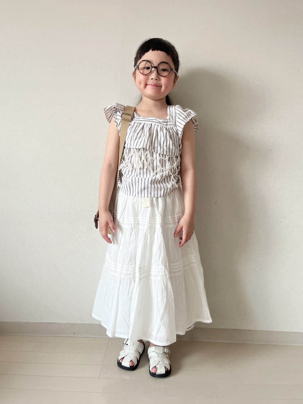 ホワイト系のスカート、ベージュ系のショルダーバッグ、ブラック系のセットアップを着用したキッズの夏コーディネートの2枚目の写真