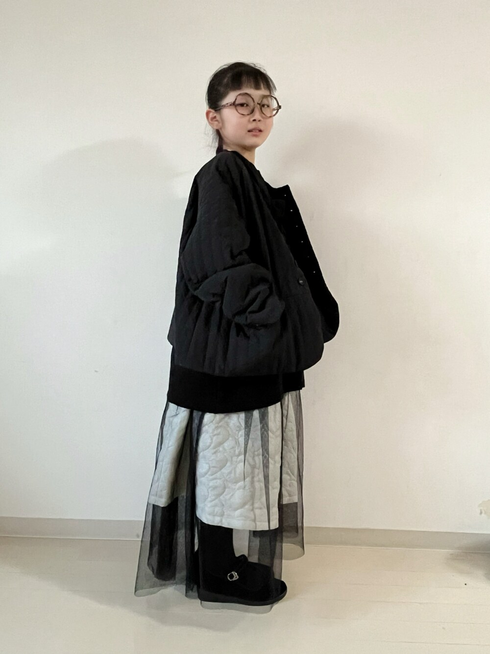 ブラック系のナイロンジャケット、ブラック系のニット/セーター、ホワイト系のスカートを着用したキッズの冬コーディネートの3枚目の写真