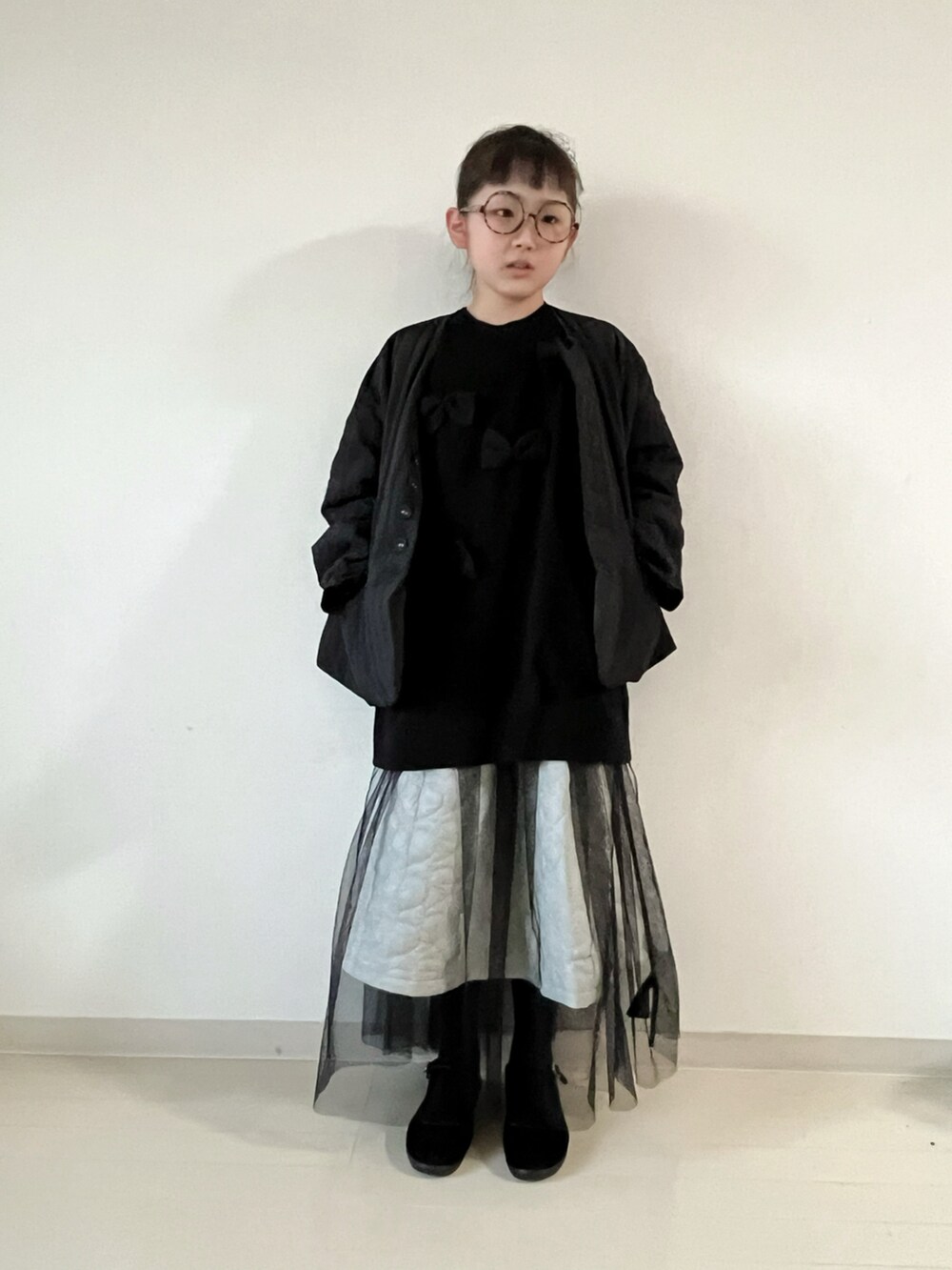 ブラック系のナイロンジャケット、ブラック系のニット/セーター、ホワイト系のスカートを着用したキッズの冬コーディネートの2枚目の写真