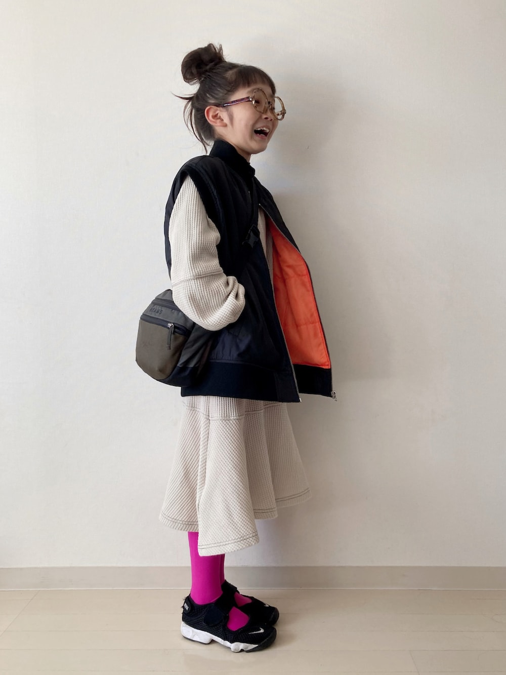 ベージュ系のワンピース、ブラック系のダウンベスト、ブラック系のスニーカーを着用したキッズの秋コーディネートの4枚目の写真