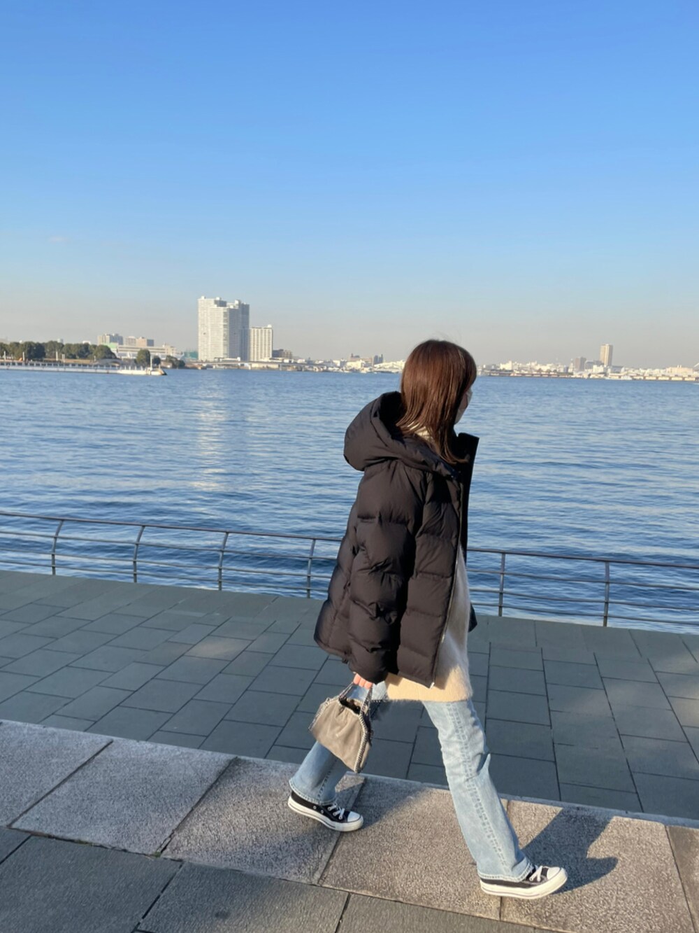 ブルー系のデニムパンツ、ブラック系のダウンジャケット/コート、ベージュ系のベストを着用したレディースの冬コーディネートの2枚目の写真