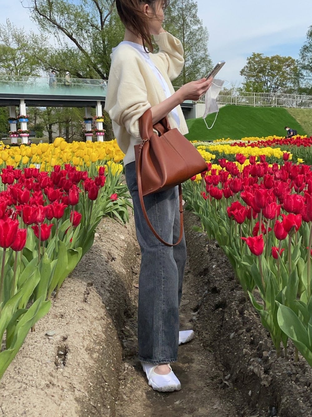 ブラック系のデニムパンツ、ベージュ系のサンダル、ブラウン系のハンドバッグを着用したレディースの秋コーディネートの2枚目の写真