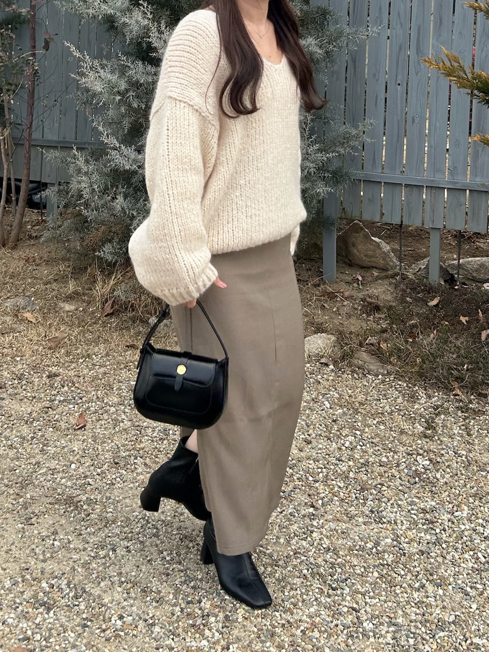 ベージュ系のスカート、ブラック系のブーツ、ブラック系のハンドバッグを着用したレディースの春コーディネートの2枚目の写真
