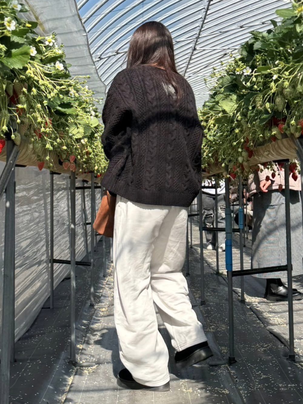 ブラック系のニット/セーター、ブラウン系のハンドバッグ、ホワイト系のスウェットパンツを着用したレディースの冬コーディネートの3枚目の写真