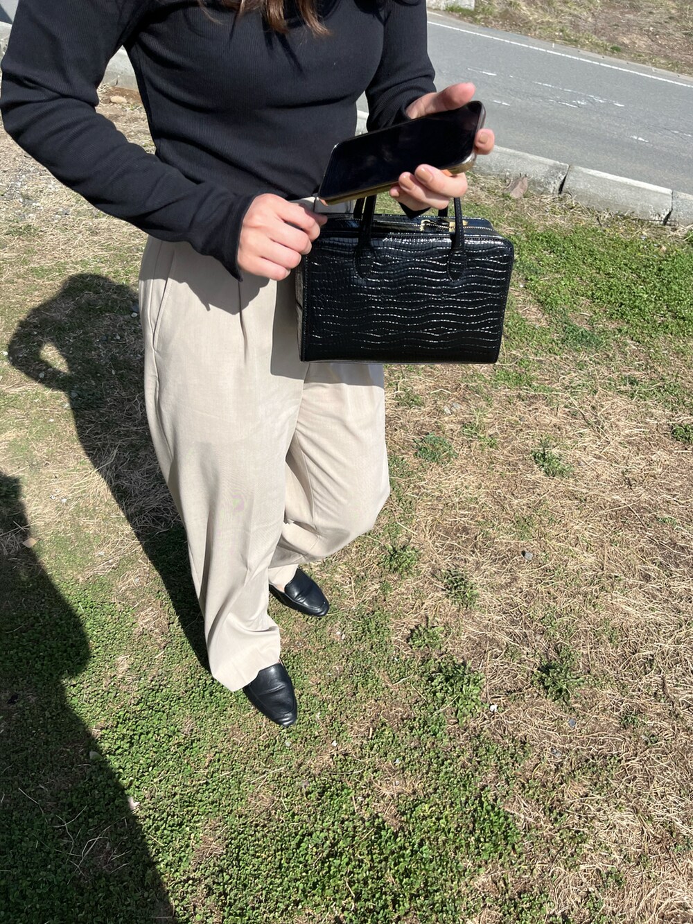 ブラック系のトップス、ベージュ系のスラックスを着用したレディースの春コーディネートの2枚目の写真