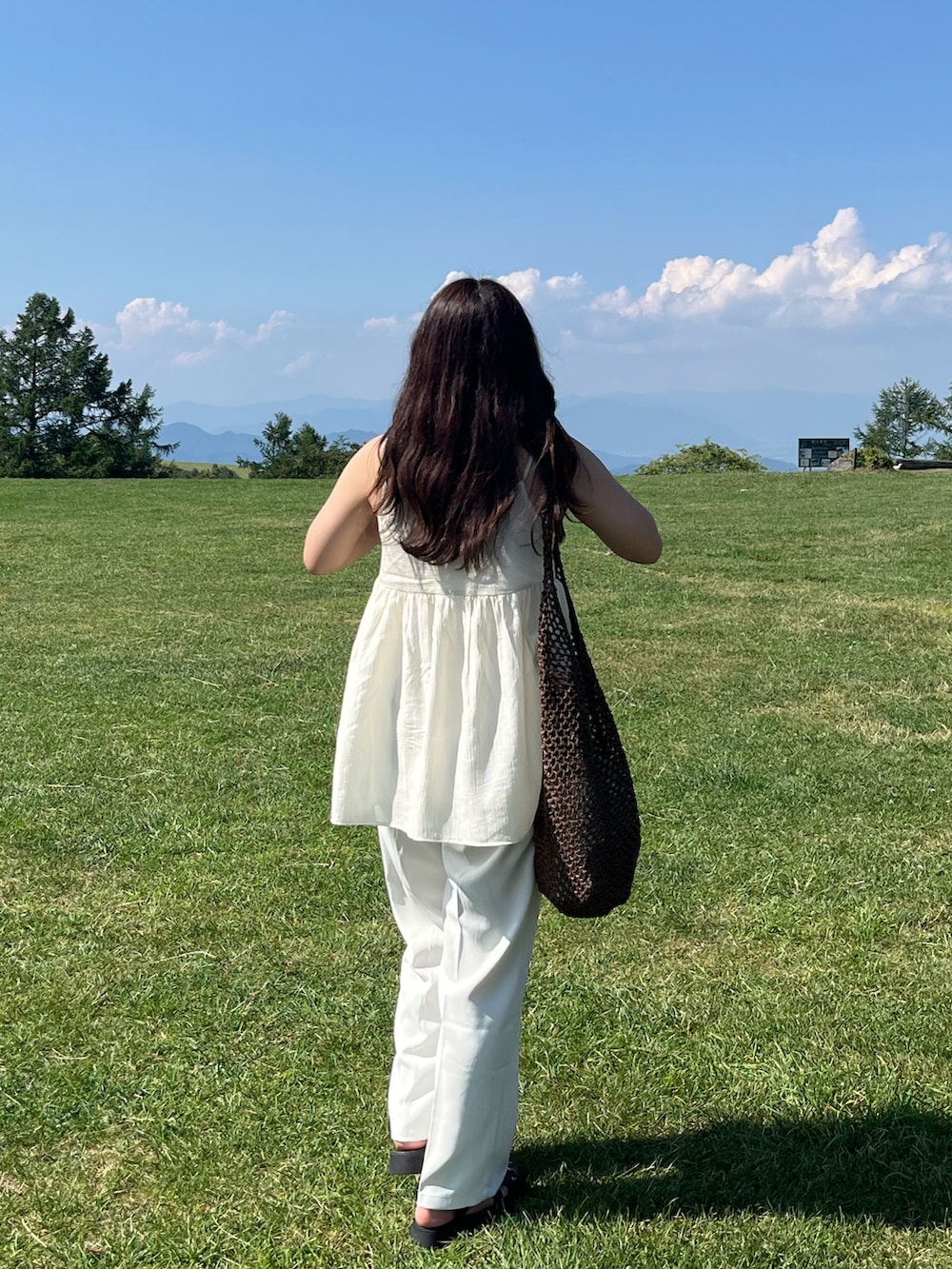 ブラウン系のショルダーバッグ、ホワイト系のスラックスを着用したレディースの夏コーディネートの2枚目の写真