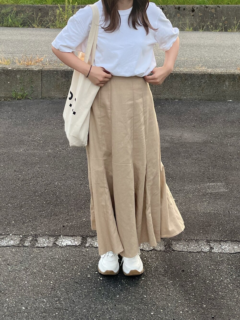 ホワイト系のトートバッグ、ベージュ系のスカート、ホワイト系のスニーカーを着用したレディースの夏コーディネートの2枚目の写真