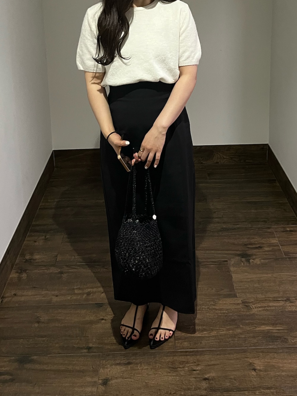 ブラック系のハンドバッグ、ホワイト系のニット/セーター、ブラック系のスカートを着用したレディースの夏コーディネートの2枚目の写真