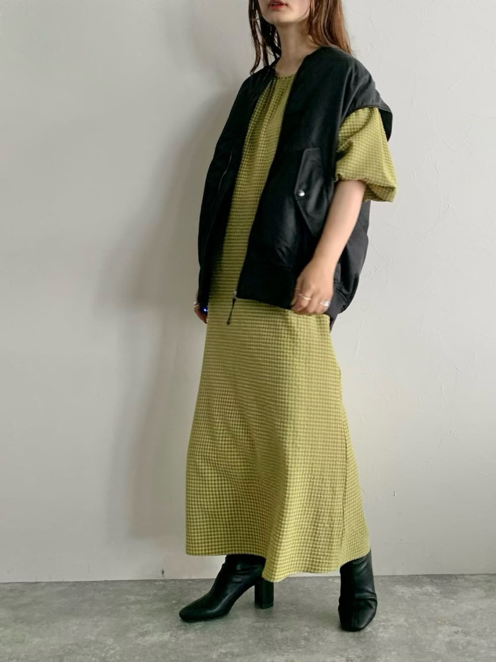 ブラック系のダウンベスト、イエロー系のワンピース、ブラック系のブーツを着用したレディースの夏コーディネートの5枚目の写真