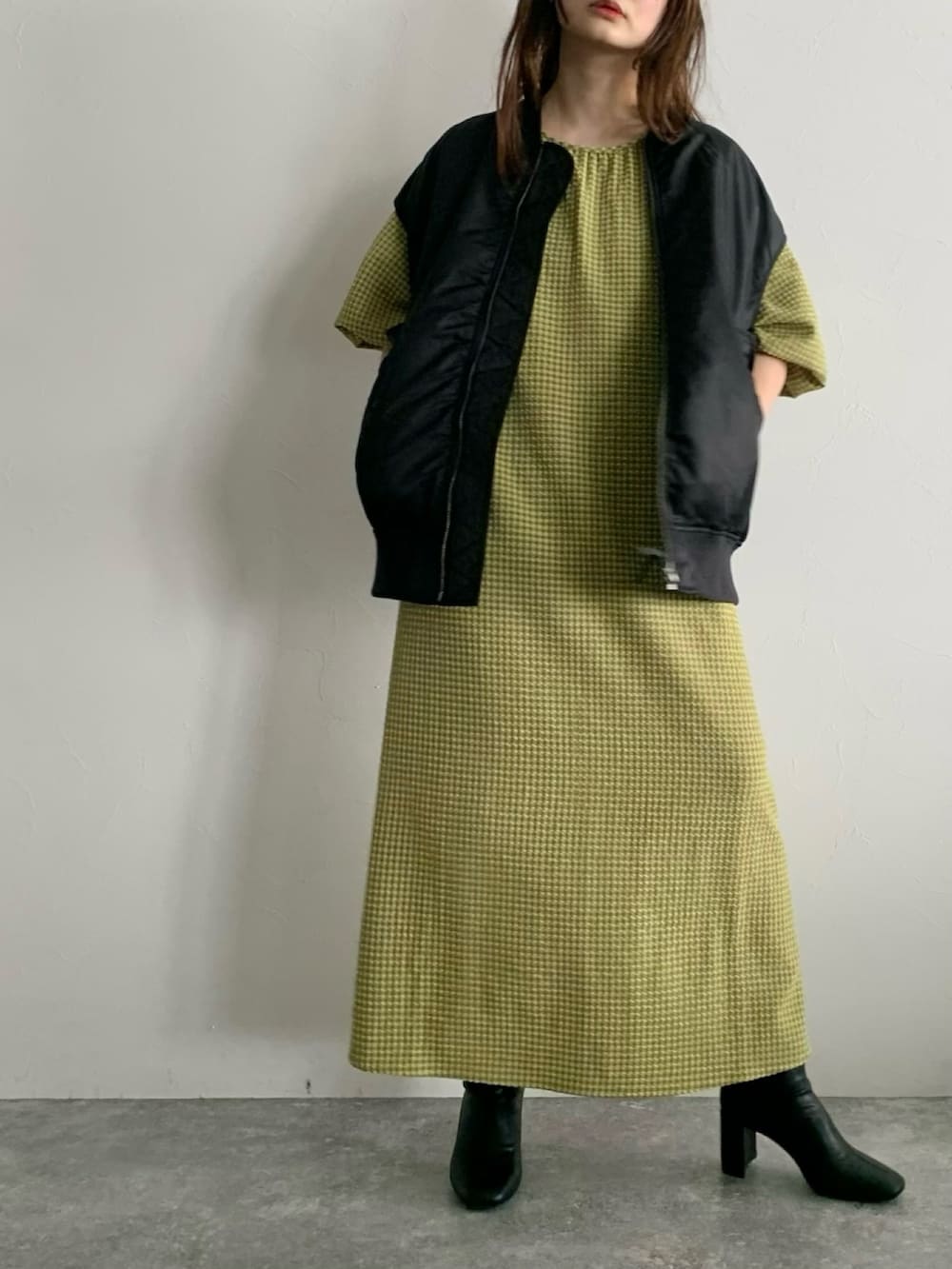 ブラック系のダウンベスト、イエロー系のワンピース、ブラック系のブーツを着用したレディースの夏コーディネートの4枚目の写真