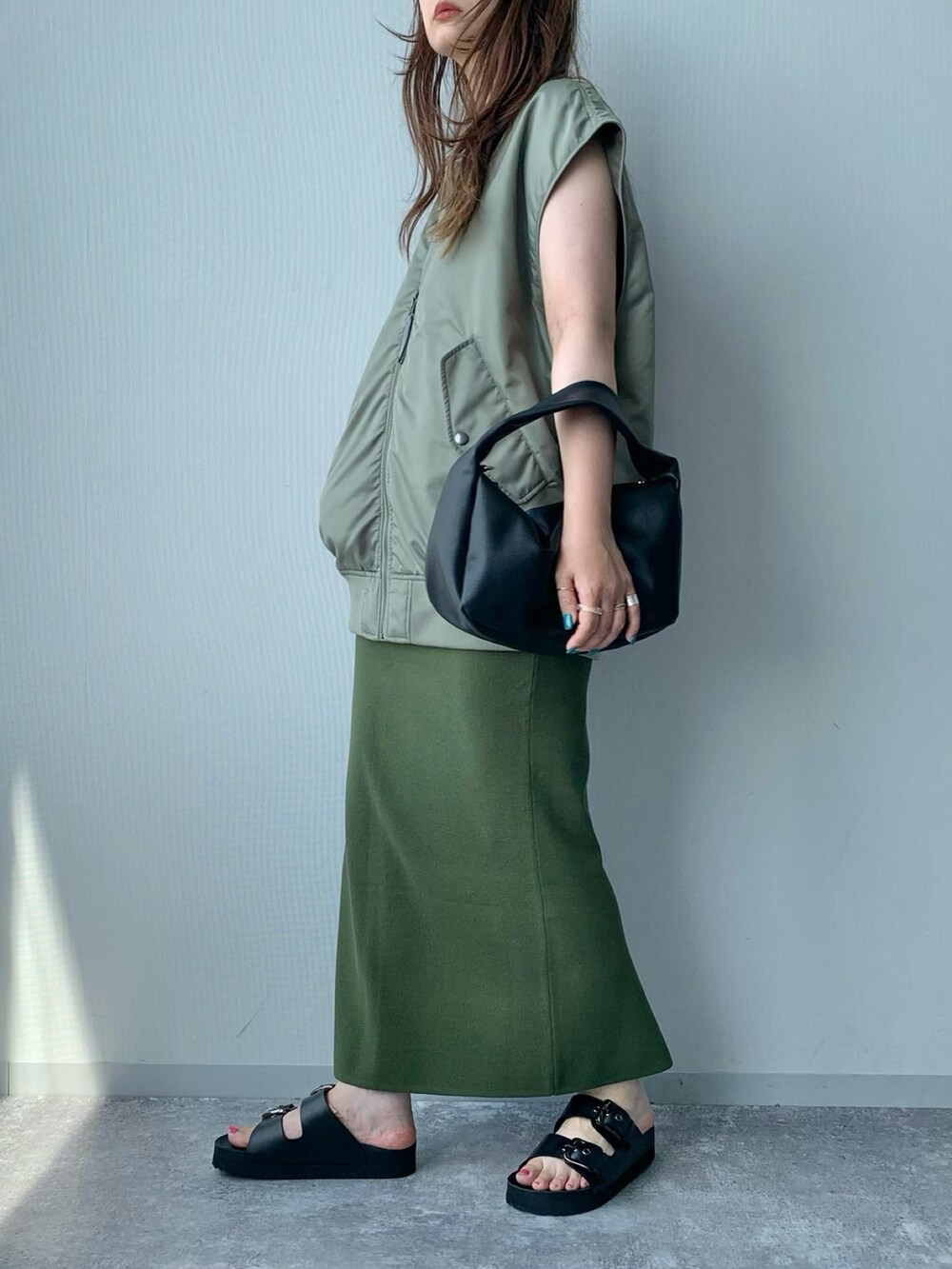 ブラック系のサンダル、グリーン系のダウンベスト、ホワイト系のショルダーバッグを着用したレディースの夏コーディネートの2枚目の写真