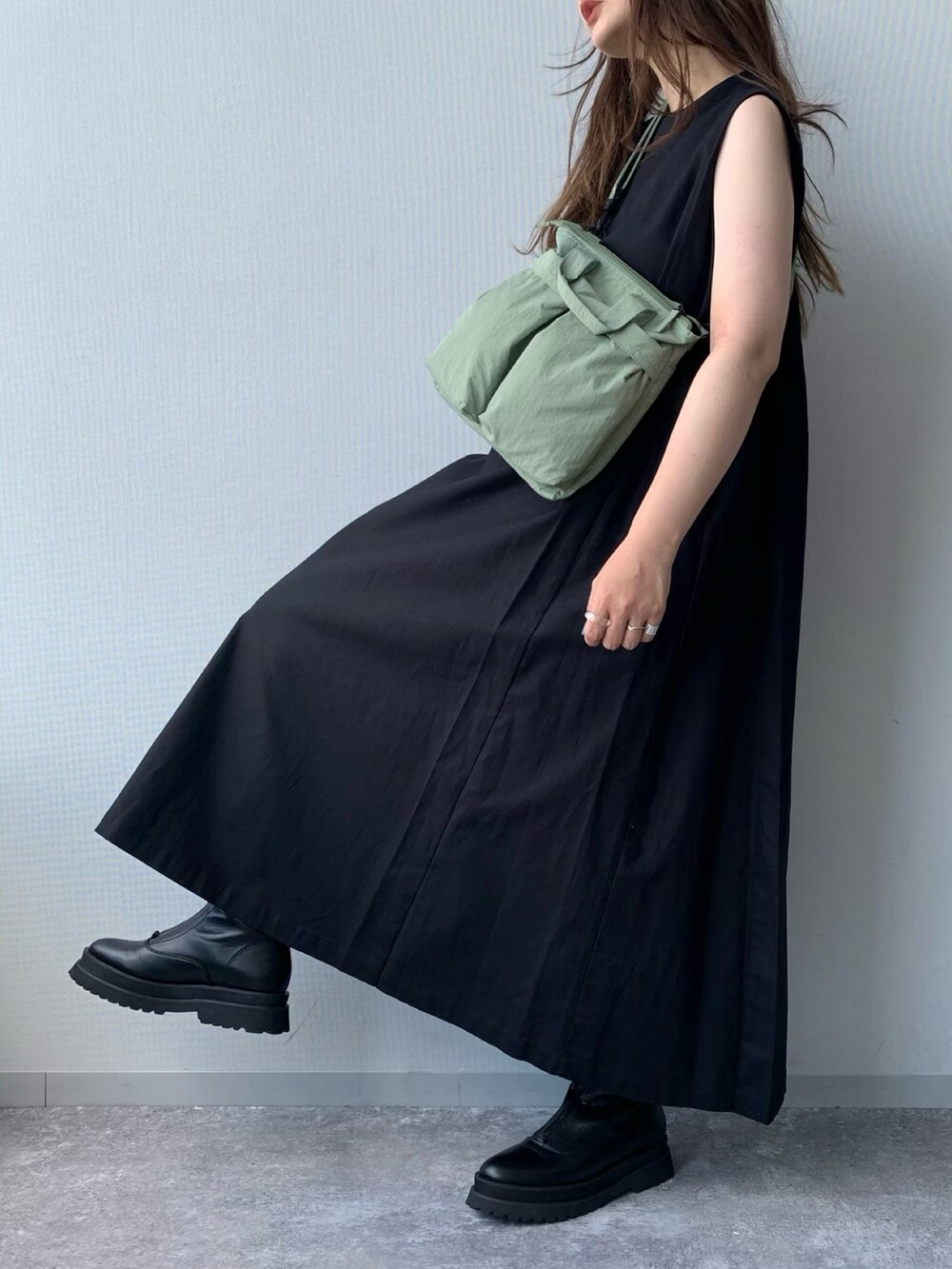 ブラック系のブーツ、ブラック系のワンピース、グリーン系のショルダーバッグを着用したレディースの夏コーディネートの2枚目の写真