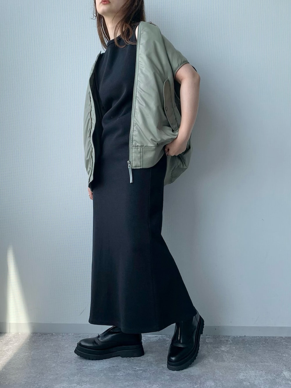 ブラック系のワンピース、ブラック系のブーツ、グリーン系のダウンベストを着用したレディースの夏コーディネートの2枚目の写真