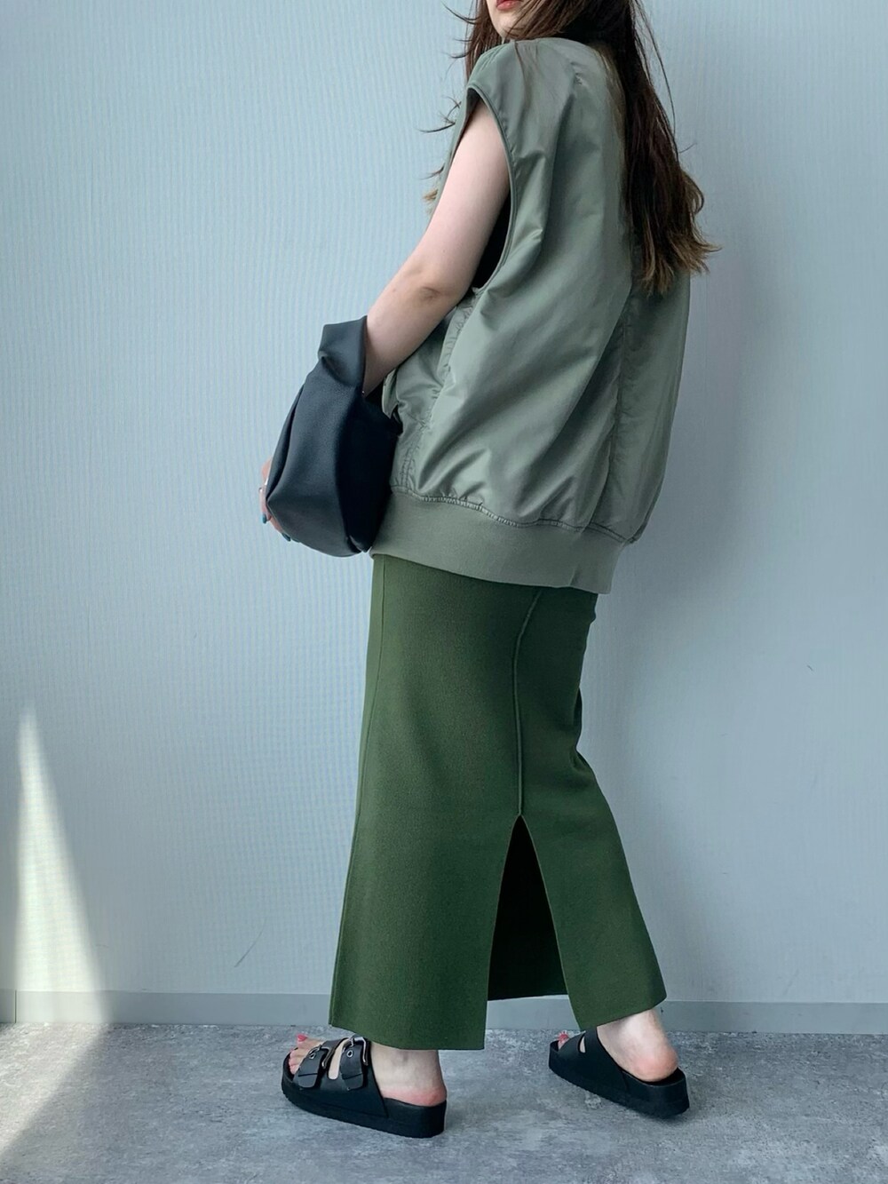 ブラック系のサンダル、グリーン系のダウンベスト、ホワイト系のショルダーバッグを着用したレディースの夏コーディネートの3枚目の写真