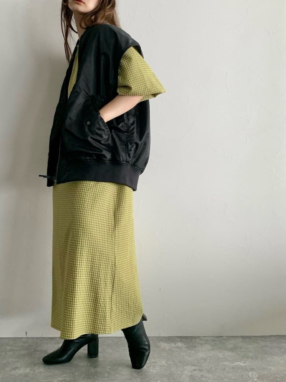 ブラック系のダウンベスト、イエロー系のワンピース、ブラック系のブーツを着用したレディースの夏コーディネートの3枚目の写真