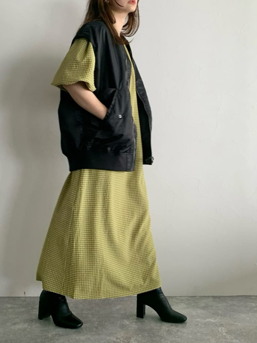 ブラック系のダウンベスト、イエロー系のワンピース、ブラック系のブーツを着用したレディースの夏コーディネートの2枚目の写真