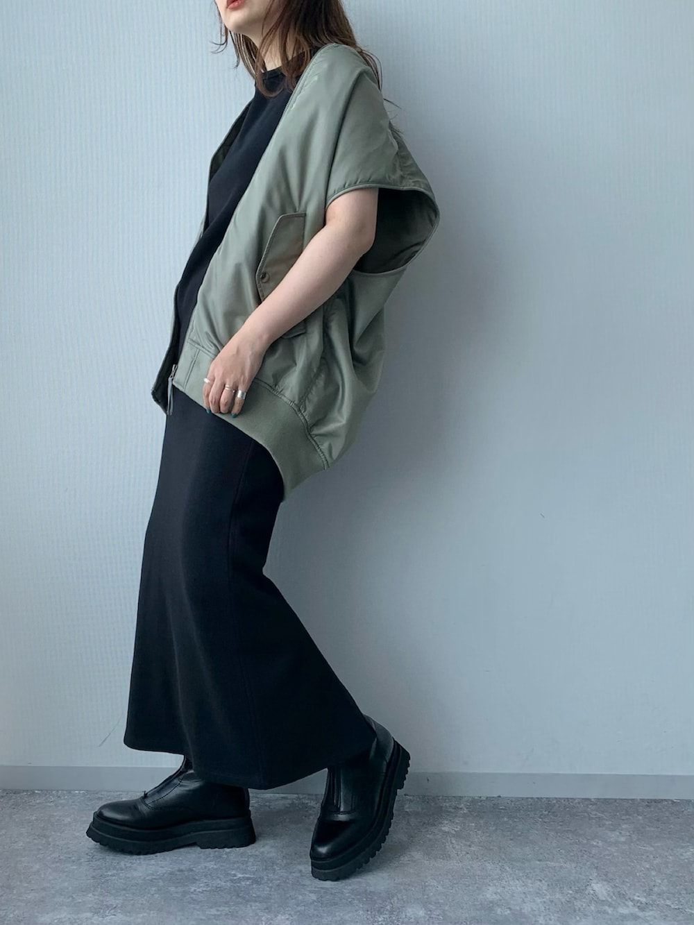 ブラック系のワンピース、ブラック系のブーツ、グリーン系のダウンベストを着用したレディースの夏コーディネートの4枚目の写真