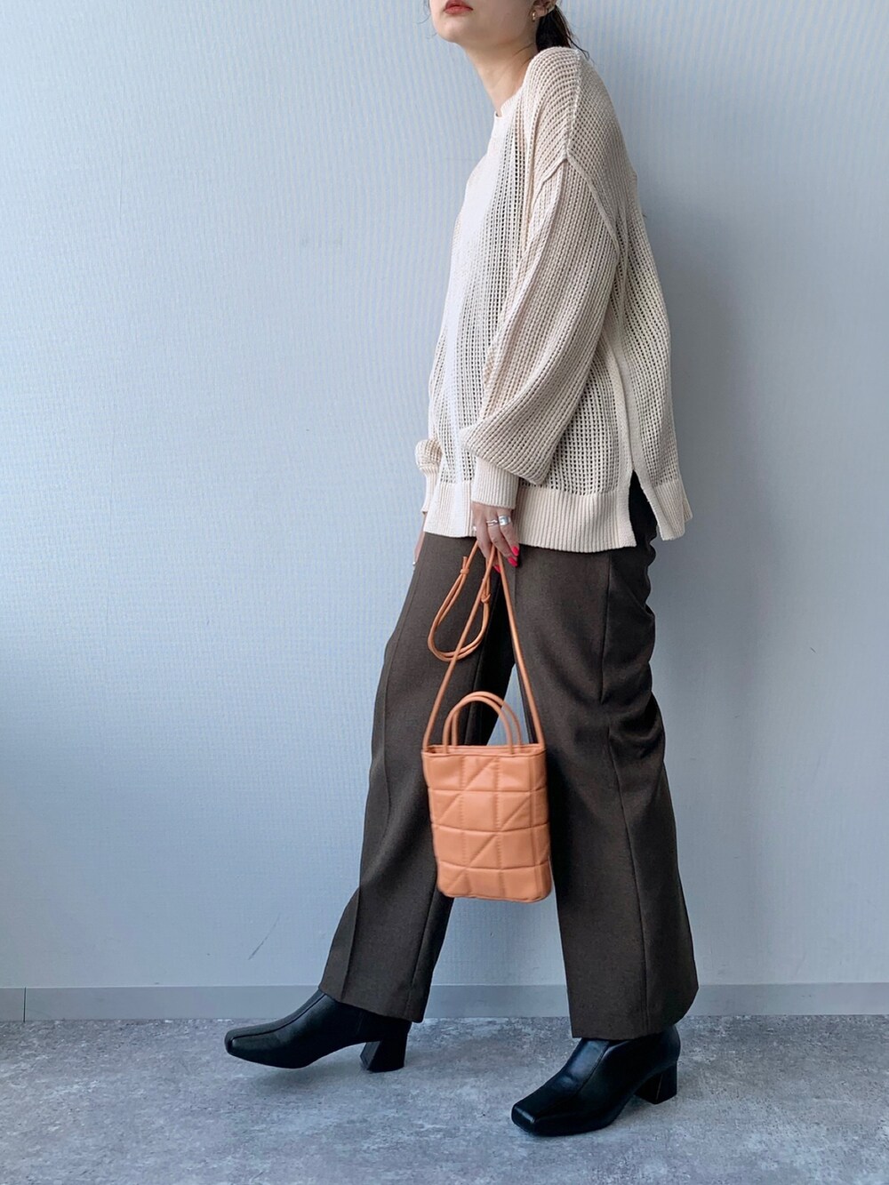 ブラック系のブーツ、オレンジ系のショルダーバッグ、ブラウン系のスラックスを着用したレディースの夏コーディネートの2枚目の写真