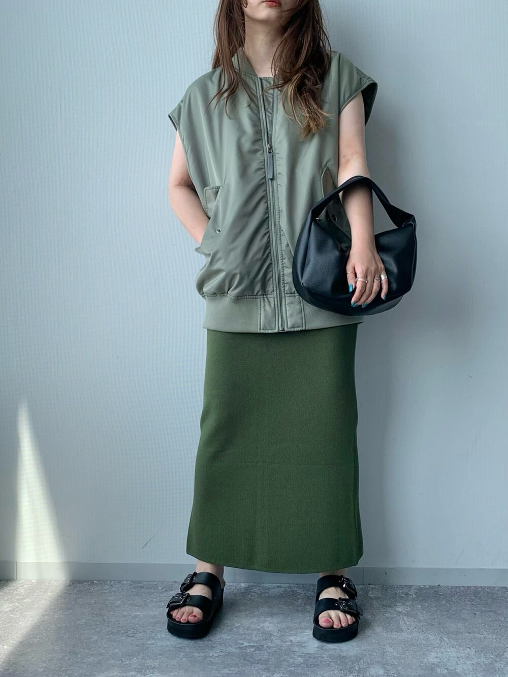 ブラック系のサンダル、グリーン系のダウンベスト、ホワイト系のショルダーバッグを着用したレディースの夏コーディネートの4枚目の写真