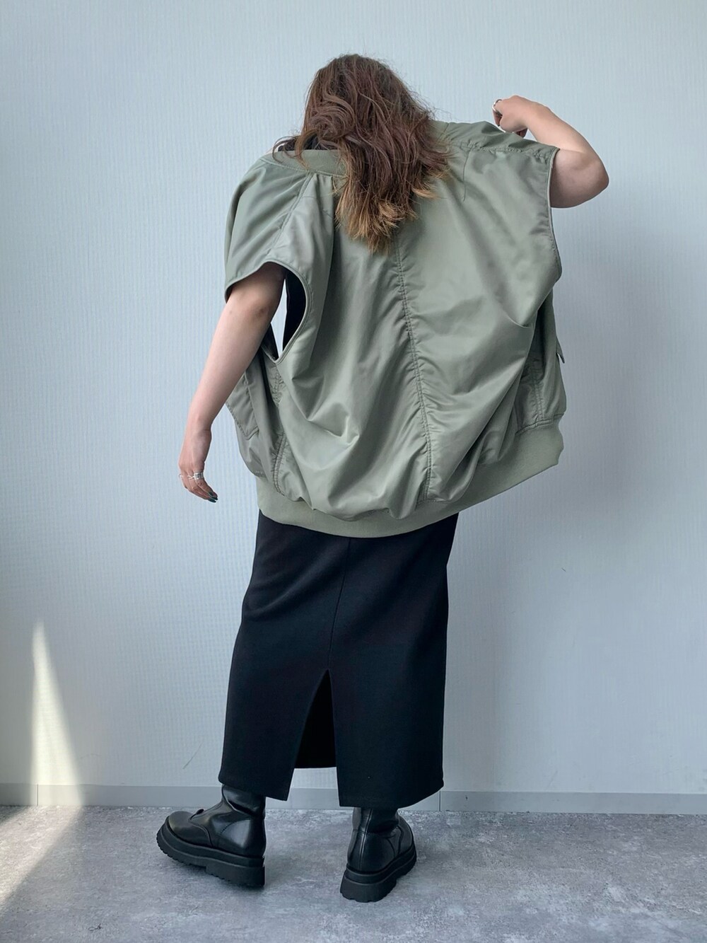 ブラック系のワンピース、ブラック系のブーツ、グリーン系のダウンベストを着用したレディースの夏コーディネートの3枚目の写真