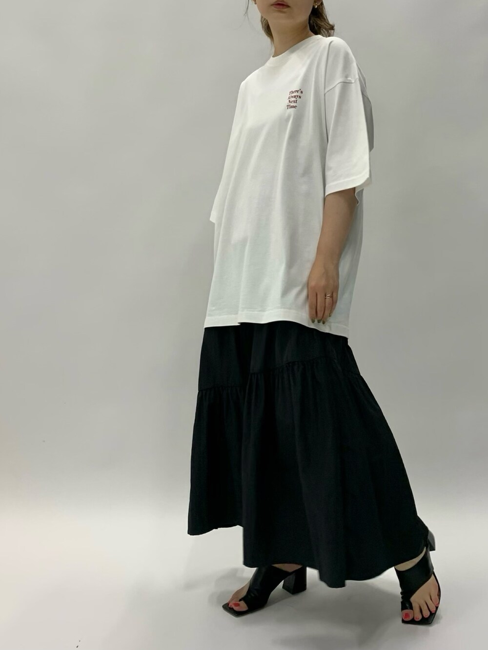 ホワイト系のトップス、ブラック系のスカート、ブラック系のサンダルを着用したレディースの夏コーディネートの2枚目の写真