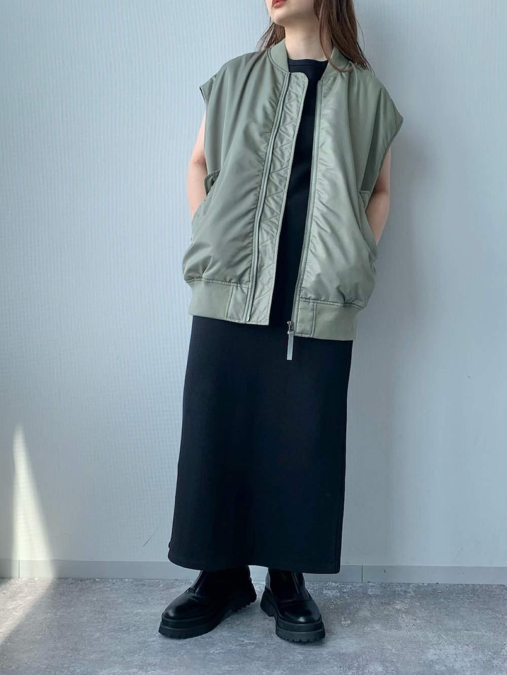 ブラック系のワンピース、ブラック系のブーツ、グリーン系のダウンベストを着用したレディースの夏コーディネートの5枚目の写真