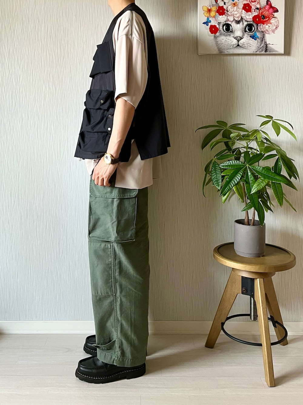 ベージュ系のTシャツ/カットソー、ブラック系のベスト、グリーン系のカーゴパンツを着用したメンズの秋コーディネートの2枚目の写真