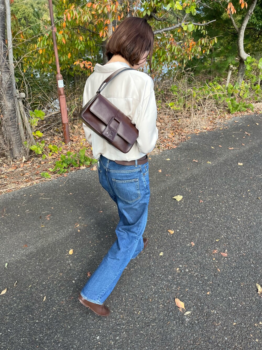 ブルー系のデニムパンツ、ブラウン系のショルダーバッグ、ベージュ系のシャツ/ブラウスを着用したレディースの秋コーディネートの2枚目の写真