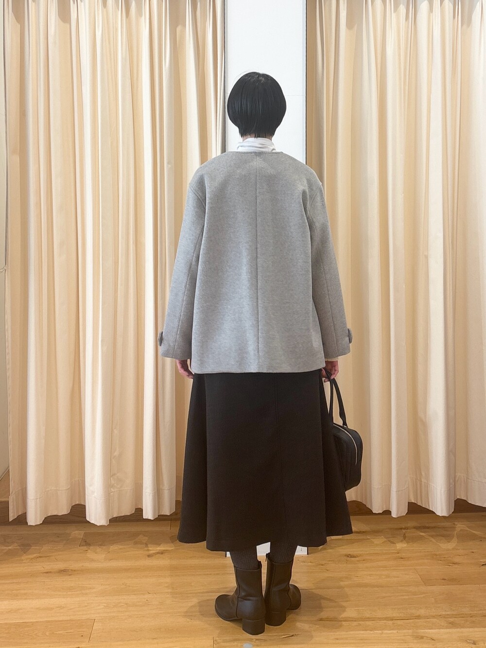 ブラック系のブーツ、ブラウン系のスカート、ブラック系のボストンバッグを着用したレディースの冬コーディネートの3枚目の写真