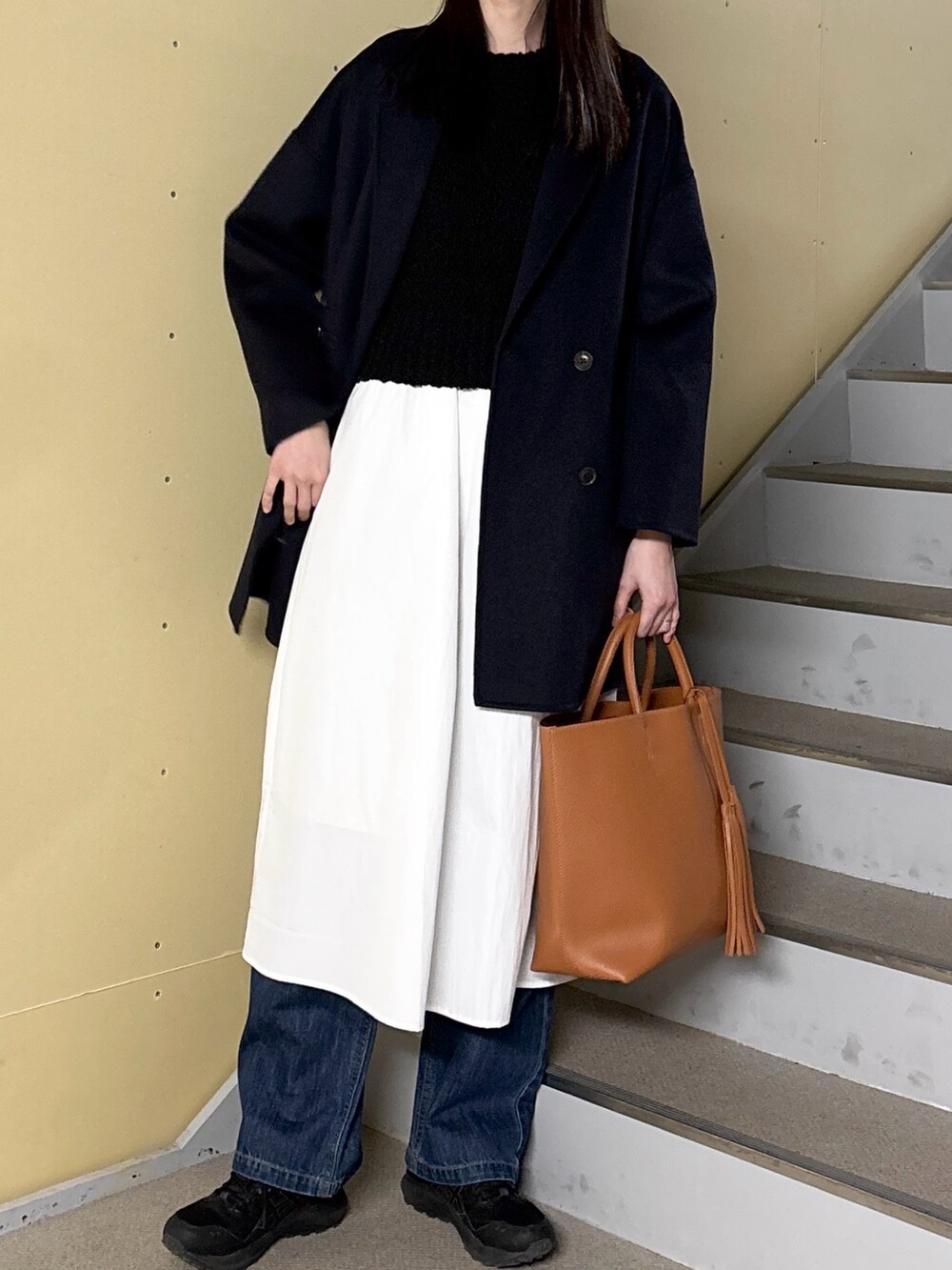 ブラック系のワンピース、ブルー系のデニムパンツ、イエロー系のトートバッグを着用したレディースの冬コーディネートの6枚目の写真