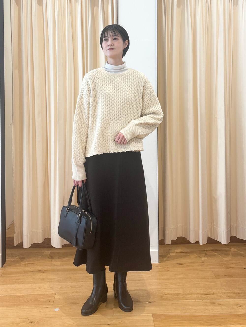 ブラック系のブーツ、ブラウン系のスカート、ブラック系のボストンバッグを着用したレディースの冬コーディネートの5枚目の写真