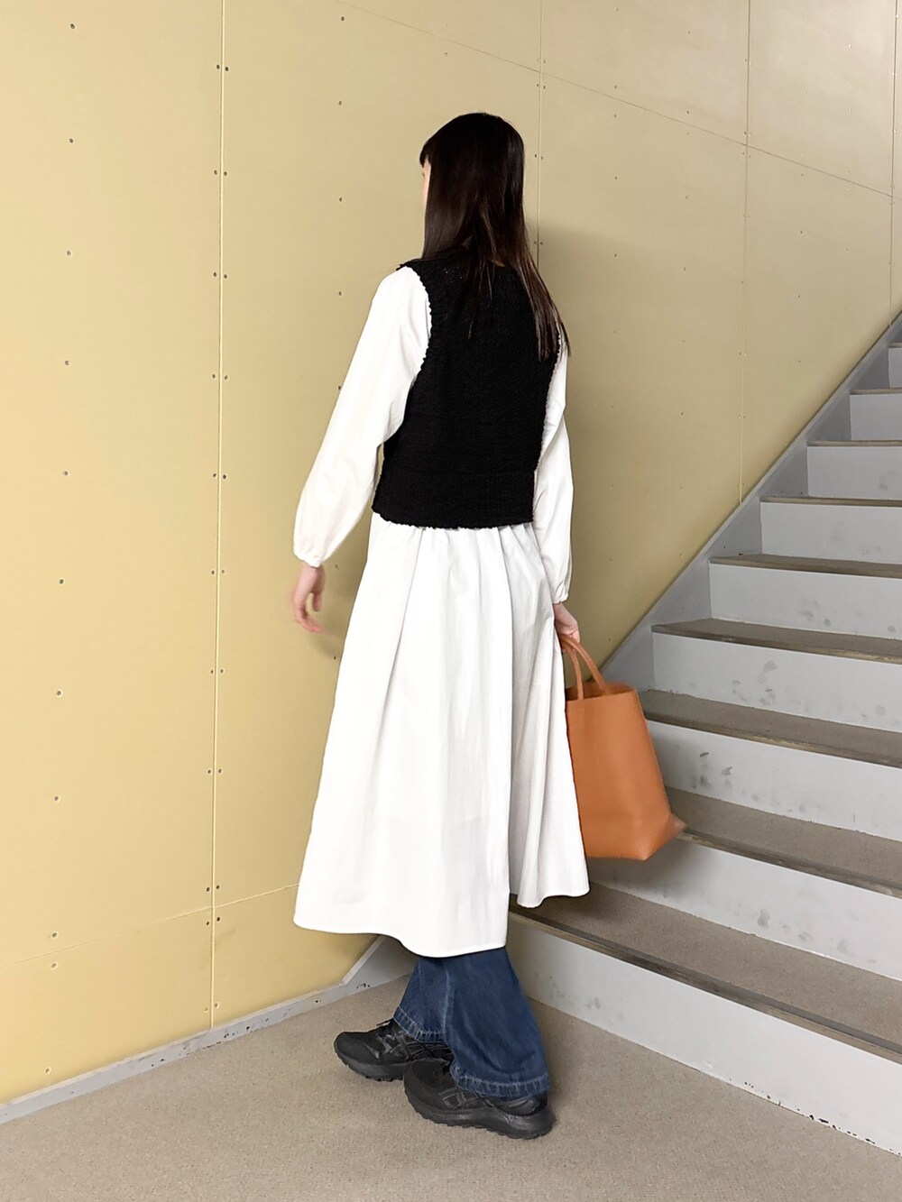 ブラック系のワンピース、ブルー系のデニムパンツ、イエロー系のトートバッグを着用したレディースの冬コーディネートの3枚目の写真